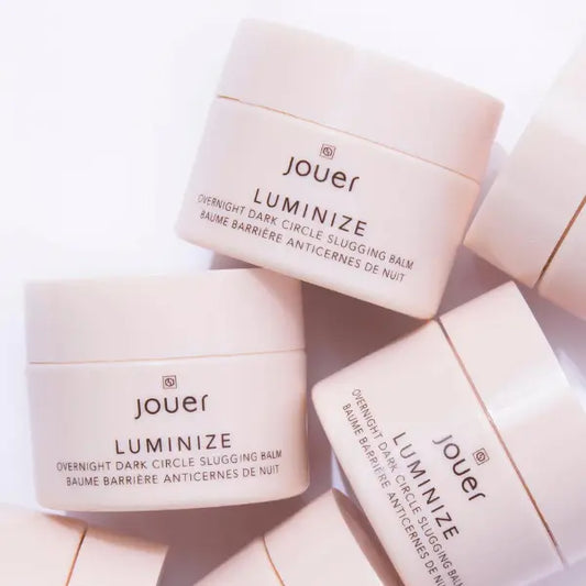 Hydrating eye treatment jars of Jouer Luminize balm displayed in soft pink packaging for overnight dark circle care.