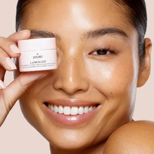 Eye balm for dark circles shown in a model’s hand with glowing, radiant skin.