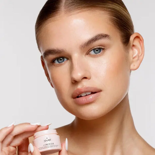 Eye balm for dark circles shown with model holding Jouer Luminize jar near radiant under-eye area.