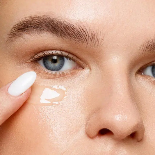 Eye cream to reduce dark circles applied under the eye with a finger on glowing, smooth skin.