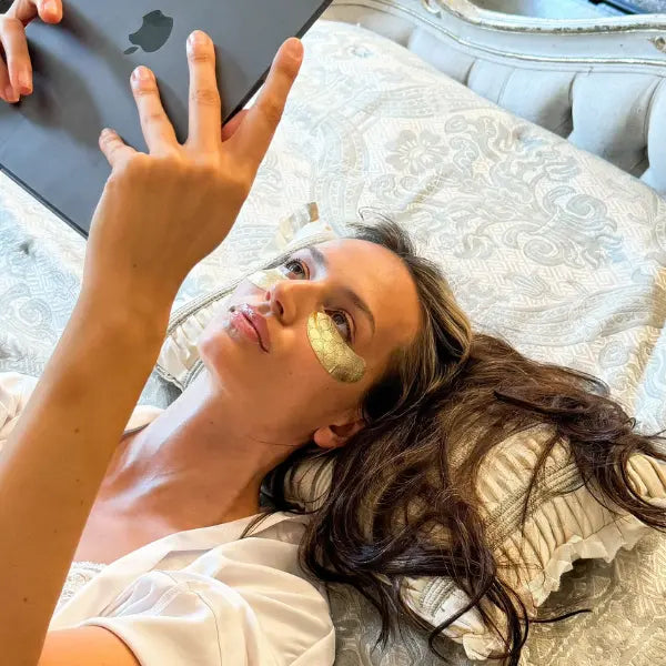 Eye mask self-care moment with gold under-eye patches while relaxing and using a tablet