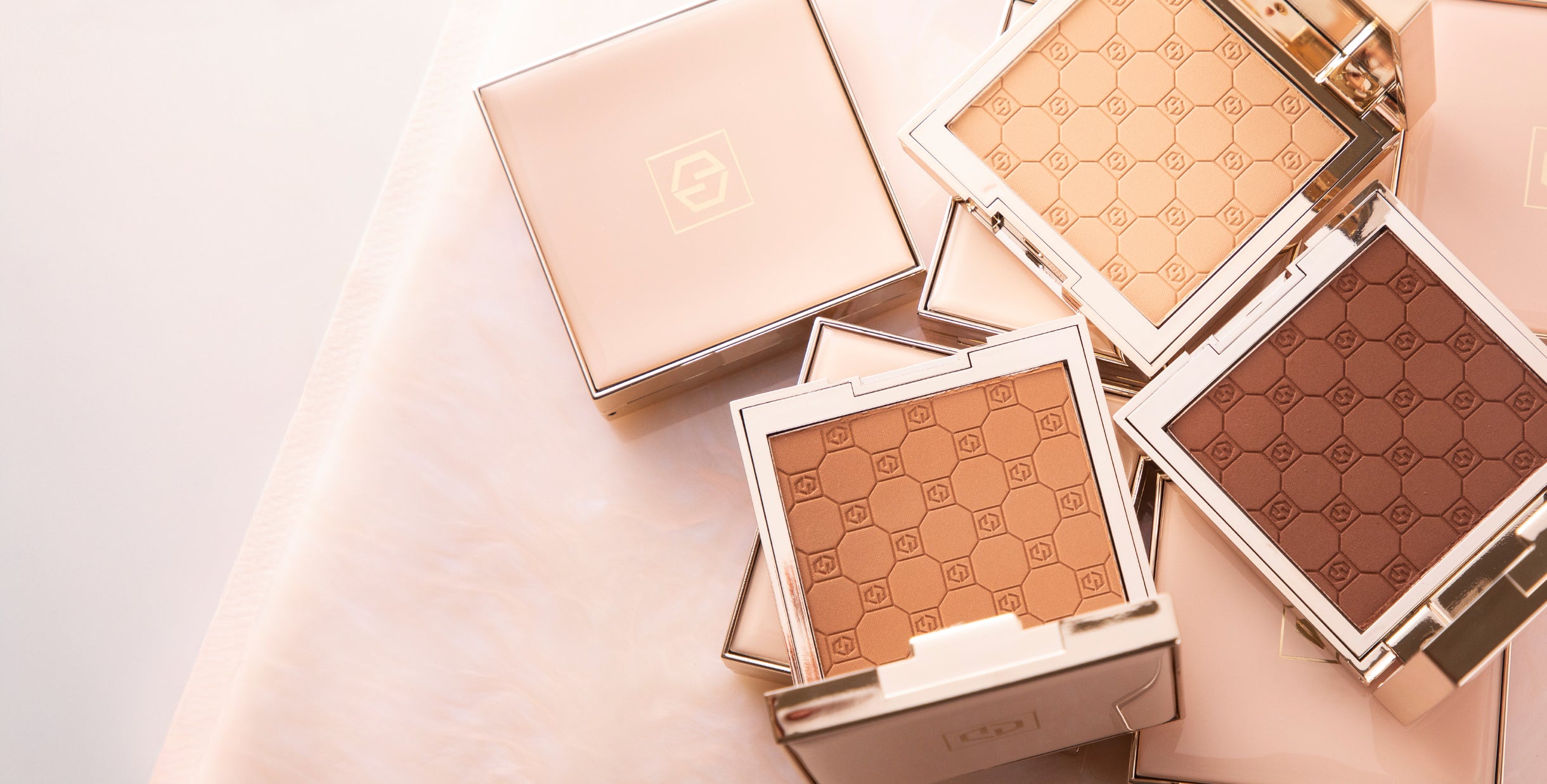Flat lay of Jouer Cosmetics' Soft focus pressed powders in luxe, gold-trimmed compacts, featuring a geometric embossed pattern on the powder surface.