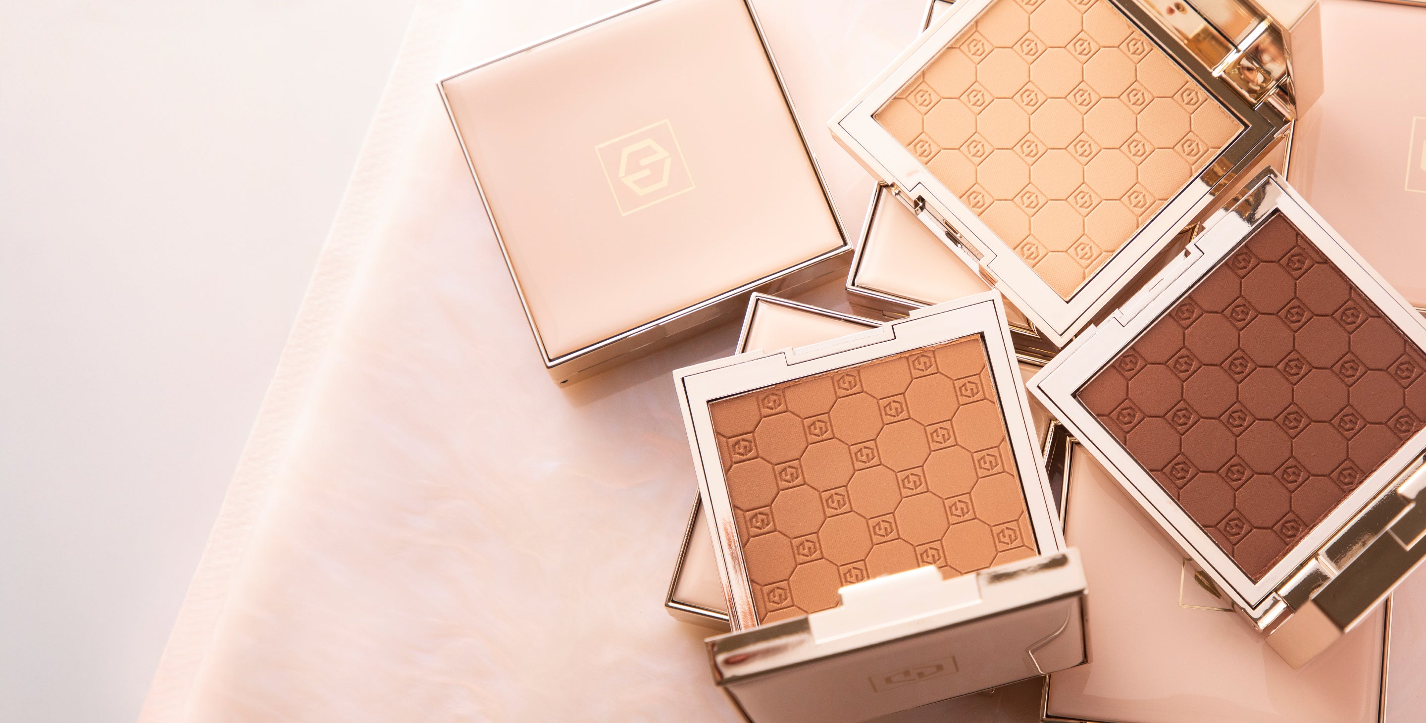 Flat lay of Jouer Cosmetics' Soft focus pressed powders in luxe, gold-trimmed compacts, featuring a geometric embossed pattern on the powder surface.