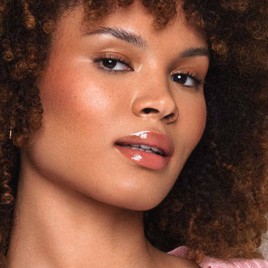 Side-by-side comparison of a woman’s face before and after makeup application. The "Before" image shows natural lips, while the "After" image displays glossy lips thanks to Jouer Cosmetics Essential Lip Oil and enhanced cheekbones, highlighting a subtle, paraben-free makeup look that accentuates her features.