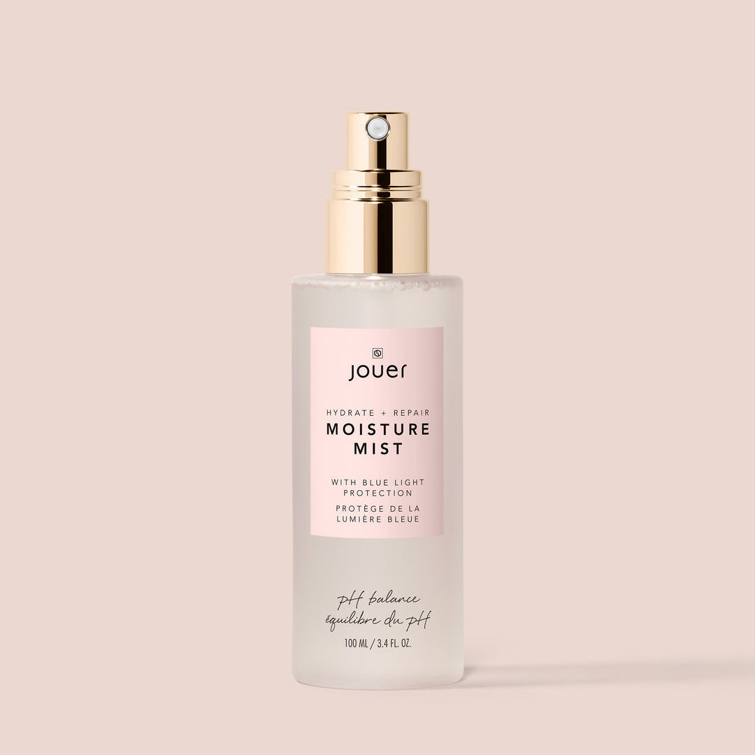 100ml, A 100ml bottle of Jouer Cosmetics' Moisture Mist, cruelty-free and vegan, is centered on a light beige background. It features a gold spray nozzle and a light pink label detailing blue light protection benefits. The text on the bottle is in English and French.