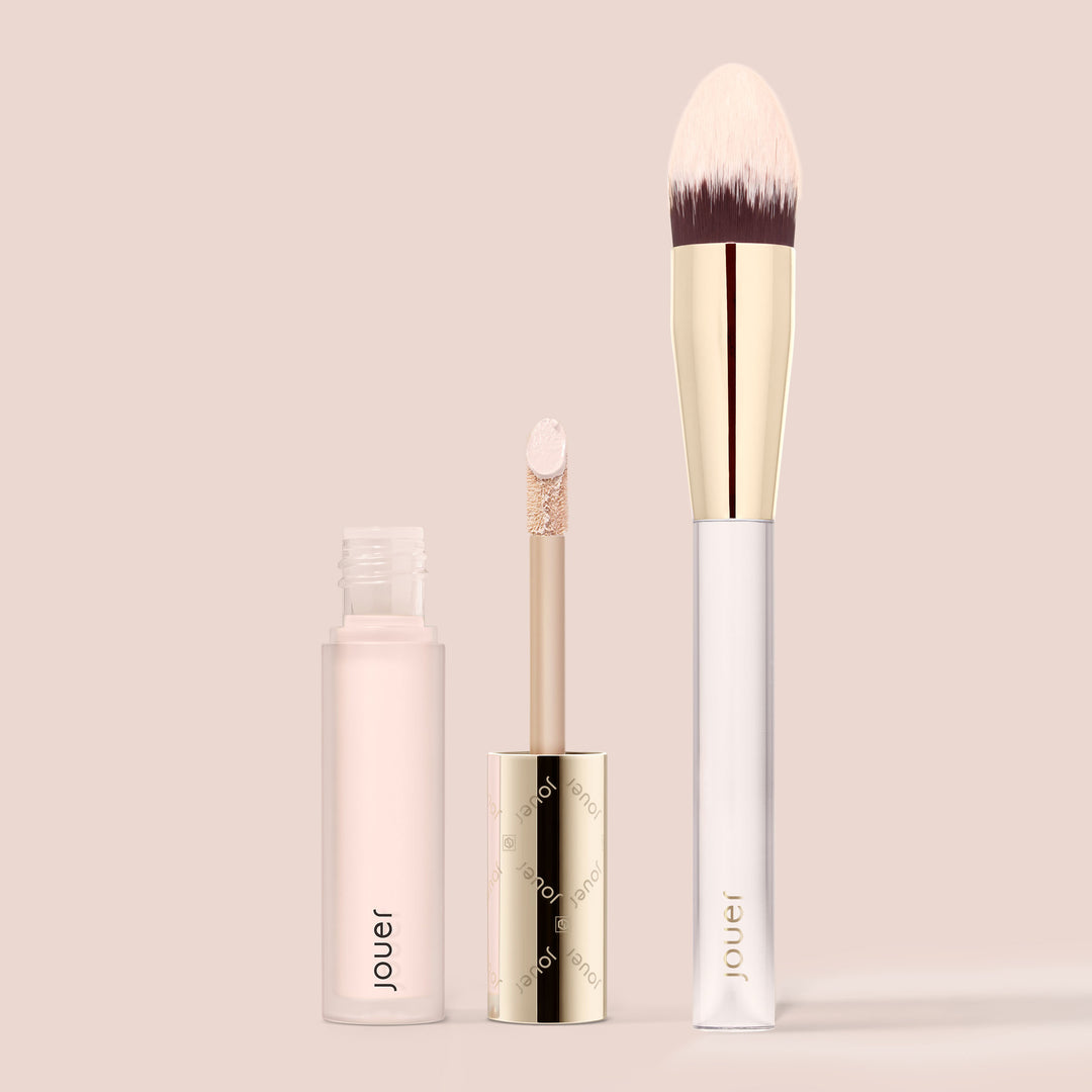 Liquid concealer and brush set in Snow, a very light neutral shade with pink undertones, featuring a doe-foot applicator and tapered blending brush on a beige background.