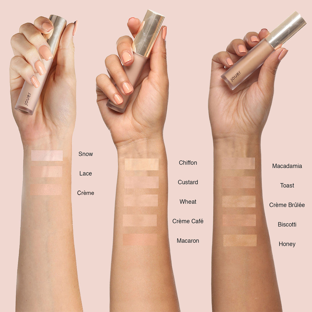 Three hands with different skin tones display swatches from the French Girl Makeup Set by Jouer Cosmetics. The left arm's swatches include Snow, Lace, and Crème. The middle arm features Chiffon, Custard, Wheat, Crème Café, and Macaron. The right arm shows Macadamia, Toast, Crème Brûlée, Biscotti, and Honey. Each hand holds a product like Liquid Concealer from Jouer Cosmetics.