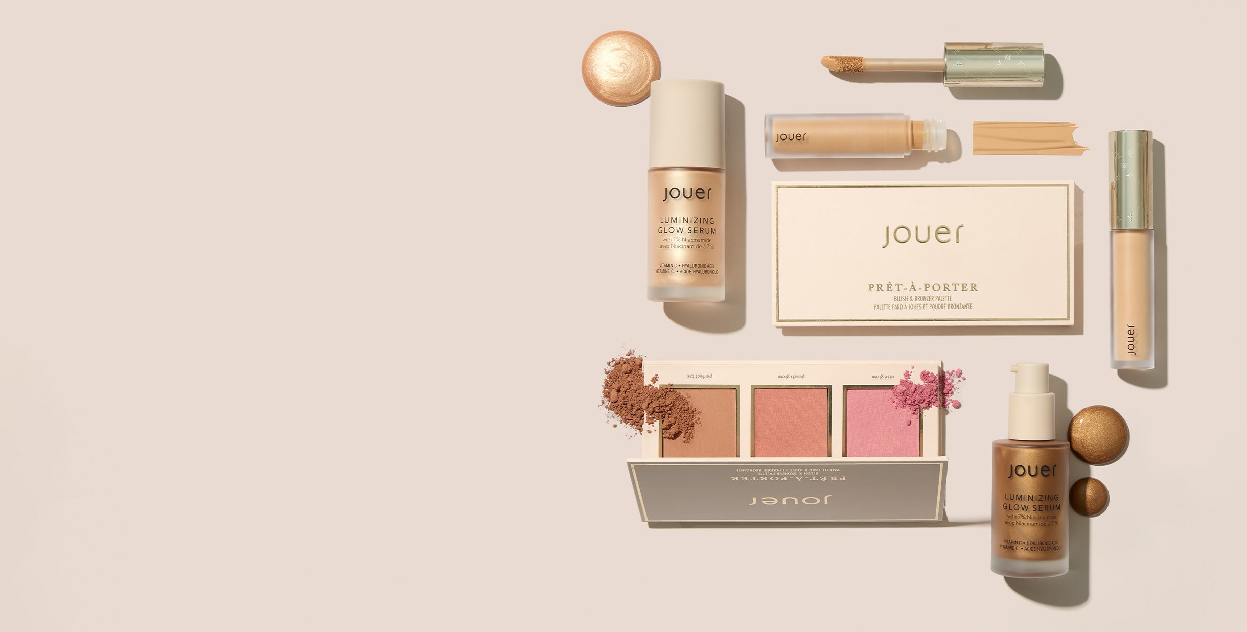 Jouer Cosmetics holiday collection displayed on a blush background—lip gloss, highlighter, blush duo, powder compact, and brush arranged side by side.