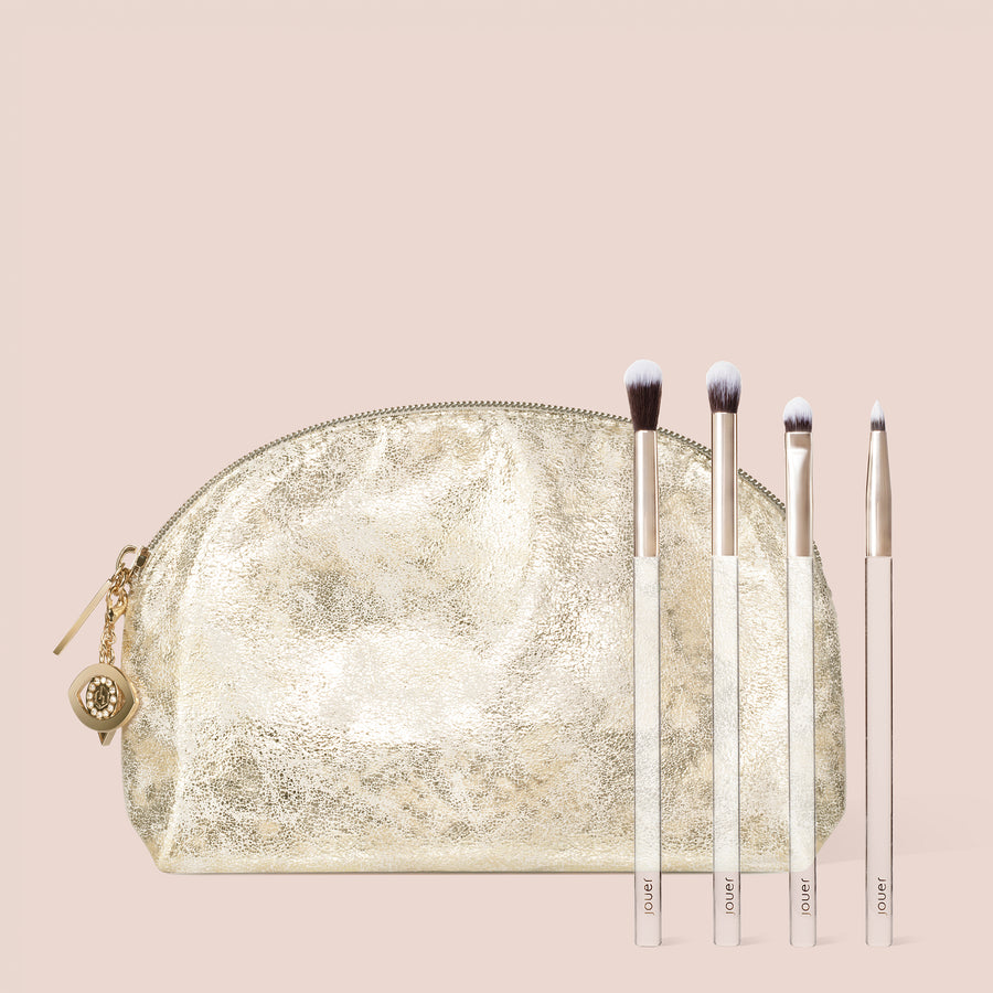 Gold cosmetic bag with four rose gold makeup brushes from Jouer's Make a Wish collection on pink background