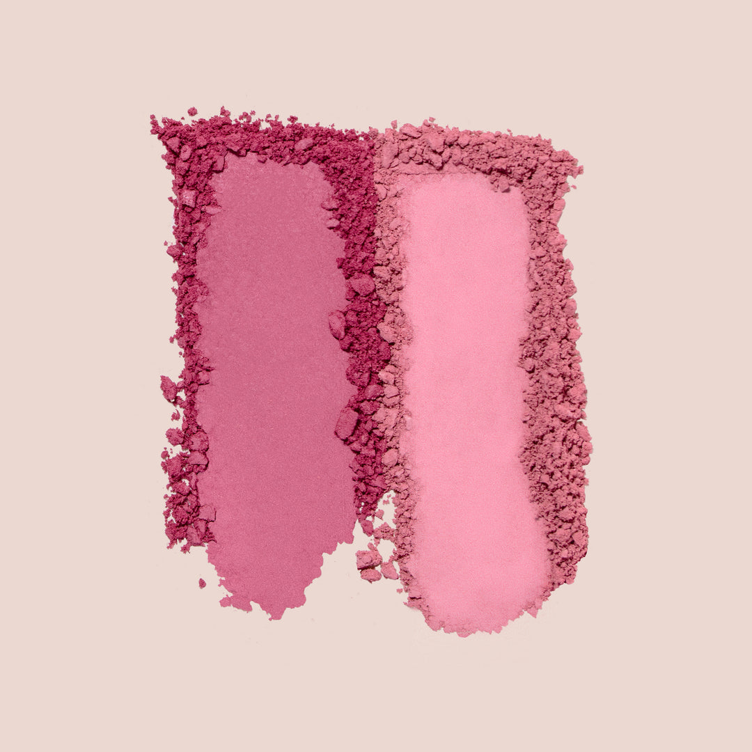 coquette, Two swatches of Jouer Cosmetics' Blush Bouquet in shades of pink. The left swatch is a deeper, dusty rose color, while the right is a lighter pastel pink. Both have a textured, powdery appearance against a beige background. These cruelty-free blushes are perfect when applied with your favorite blush brush.