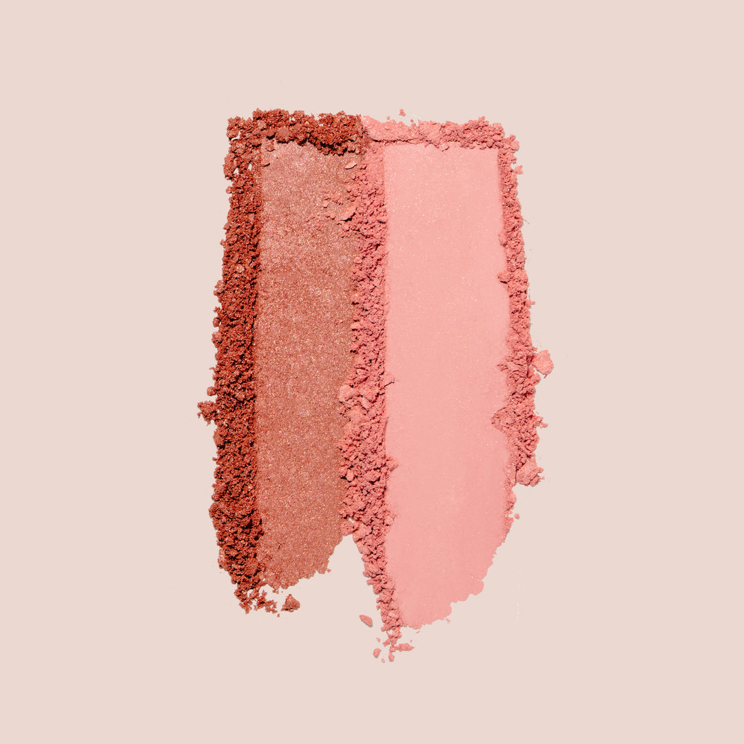 Two vertical swatches of the Mini Blush Bouquet by Jouer Cosmetics are displayed. The left swatch is a shimmery, darker coral shade, ideal for achieving a natural flush. In contrast, the right swatch is a matte, lighter pink shade. Both paraben-free swatches have slightly crumbly edges against a light beige background.