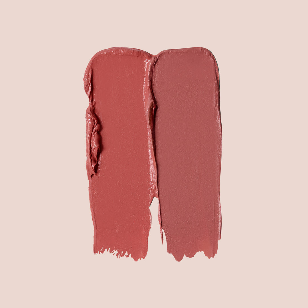 Celebrate, Two swatches of Blush & Bloom vegan lipstick by Jouer Cosmetics in different shades of pink are displayed on a light beige background. The left swatch is a slightly darker, more coral pink, while the right swatch is a softer, muted pink. Both cruelty-free swatches have a creamy texture.