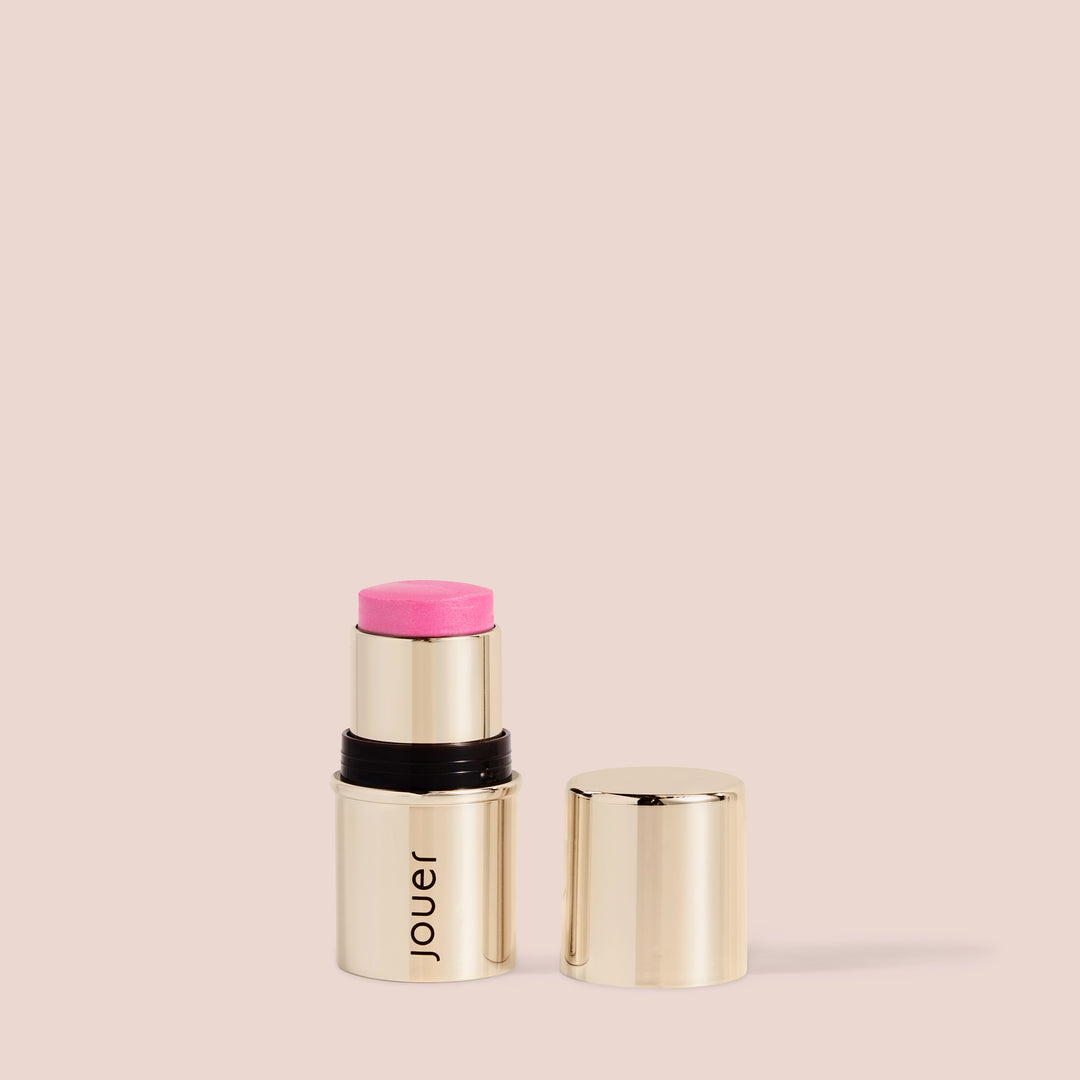 Peony, A gold tube of Jouer Cosmetics Blush & Bloom blush stick with its cap off, revealing a pink, vegan blush tip. The paraben-free product is set against a clean beige background. The Blush & Bloom stands upright, with the removed cap placed beside it.