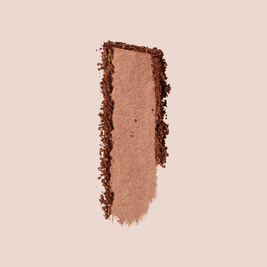  A swatch of metallic bronze powder from Jouer Cosmetics' Ménage à Trois Set is pressed vertically on a light beige background, showcasing its shimmery texture and rich color. The edges are slightly uneven, highlighting the product's powdery consistency. The Menage a Trois powder is a three-in-one butter bronzer, highlighter and blush. This vegan formula is paraben-free for a cleaner beauty choice.