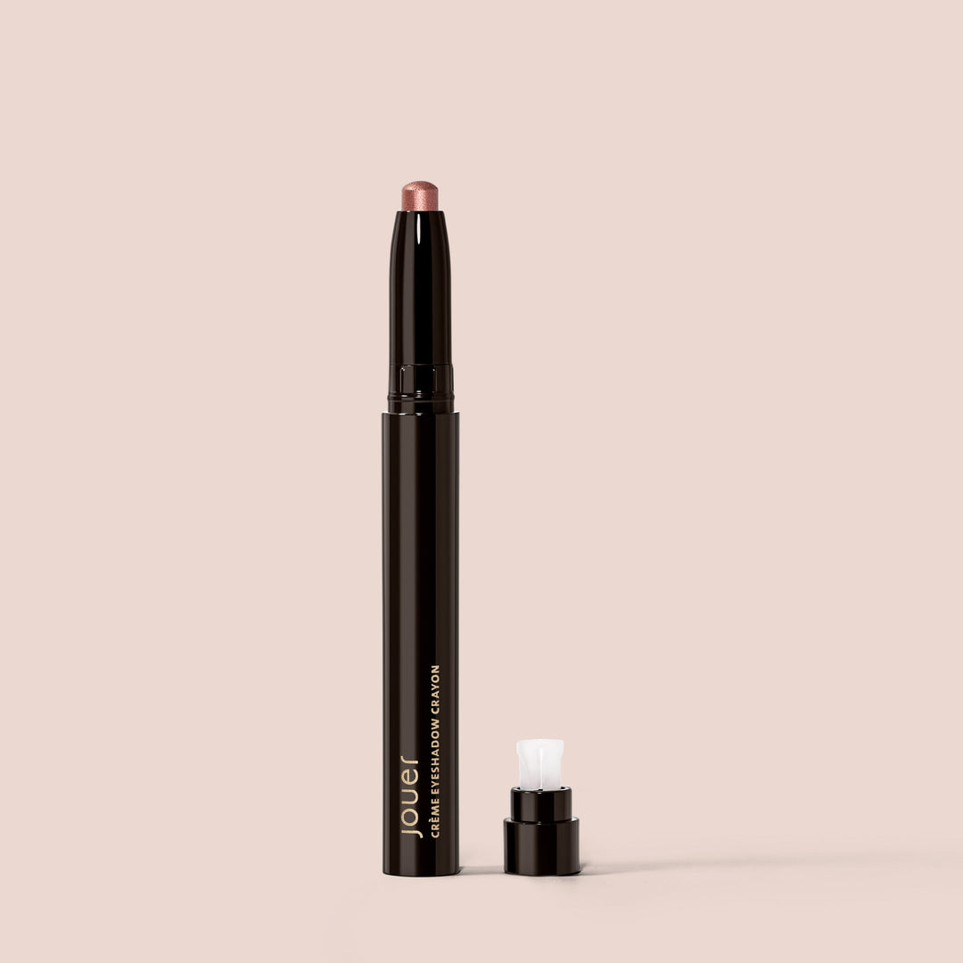 Jouer cream eyeshadow crayon in rose gold shade with black packaging and cap removed on beige background