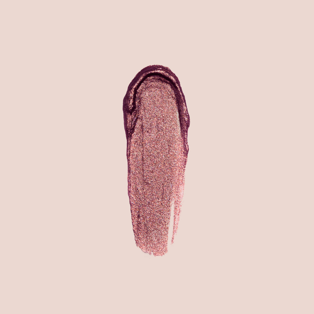Desir, The Paris Lights Eye Paint from Jouer Cosmetics features a creamy and smooth swatch of makeup that blends a shimmering rose gold with deep plum colors on a light beige background. This luxurious product is both paraben-free and vegan, offering an ethical choice for your beauty routine.