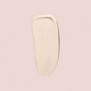  A close-up of a smear of Essential Crème Foundation by Jouer Cosmetics on a light beige background. The smooth and slightly glossy texture suggests that this paraben-free product is likely a luxurious cosmetic foundation. The elongated shape with rounded edges further highlights its creamy consistency.