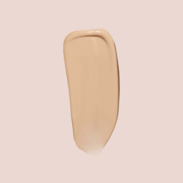  A brush stroke of Jouer Cosmetics' Essential Crème Foundation, which is cruelty-free and paraben-free, is displayed against a light, neutral background. The texture appears smooth and creamy, showcasing a glossy finish.
