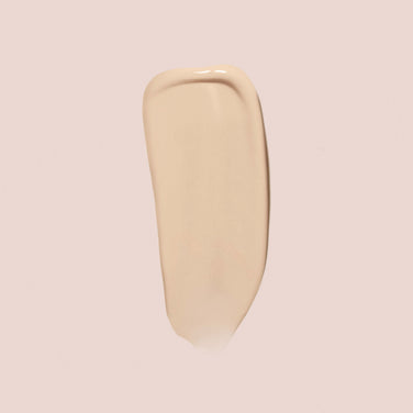  A smooth swatch of Jouer Cosmetics' Essential Crème Foundation in a beige hue is displayed on a light, neutral background. The swatch boasts a slightly glossy texture and appears even and uniform with a single stroke. Additionally, it’s cruelty-free, making it a conscientious choice.