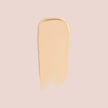  A smooth, light beige smear of Jouer Cosmetics' Essential Crème Foundation is set against a light taupe background. The foundation appears creamy in texture with a slight sheen, indicating a moist application. This cruelty-free product ensures beauty without compromise.