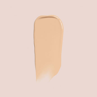  A swatch of Essential Crème Foundation by Jouer Cosmetics on a light peach-colored background, showcasing the texture and smooth consistency of this cruelty-free cosmetic product.