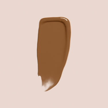  A thick swatch of Jouer Cosmetics' Essential Crème Foundation, which is both paraben-free and cruelty-free, is displayed on a light beige background. The swatch has smooth edges on the top and sides, with a slightly uneven edge at the bottom. The texture appears to be smooth and glossy.