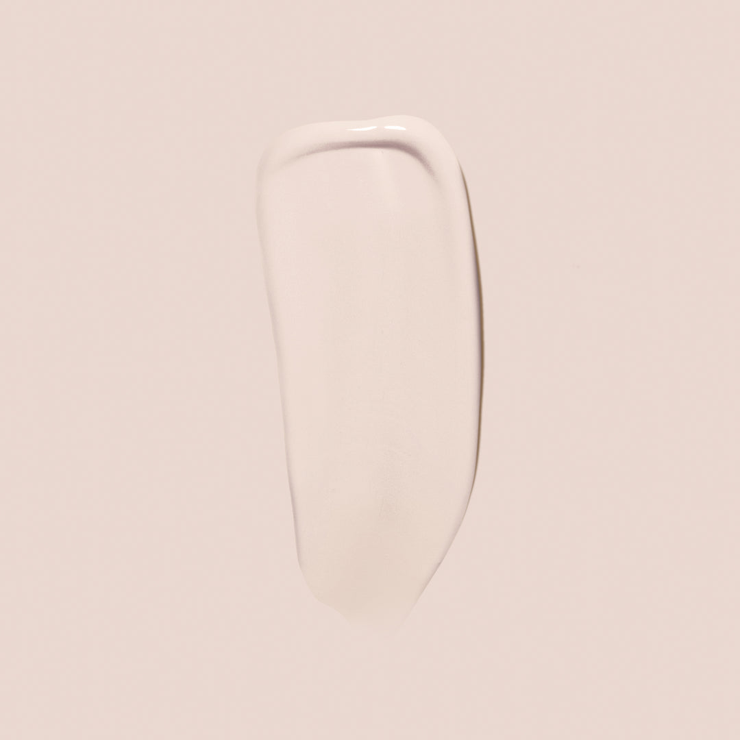 ivory, full size alt: A light beige, smooth, creamy substance—identified as Essential Crème Foundation from Jouer Cosmetics—is spread in an elongated, slightly curved shape on a pale background. The texture appears glossy and somewhat opaque, suggesting it is a high-quality cruelty-free skincare or cosmetic product.