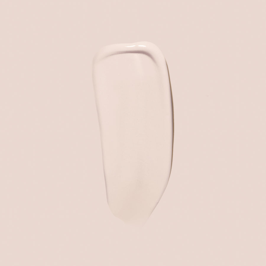 ivory, full size alt: A light beige, smooth, creamy substance—identified as Essential Crème Foundation from Jouer Cosmetics—is spread in an elongated, slightly curved shape on a pale background. The texture appears glossy and somewhat opaque, suggesting it is a high-quality cruelty-free skincare or cosmetic product.