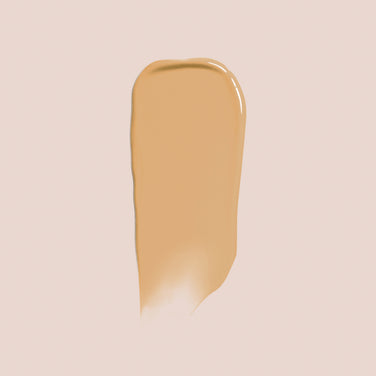  A swatch of Jouer Cosmetics Essential Crème Foundation, a paraben-free liquid formula in beige, is smeared on a light background to showcase its texture and color. The foundation has a smooth and creamy consistency with subtle variations in shading that highlight its slightly glossy finish.