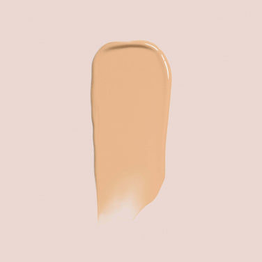  A swipe of light beige Essential Crème Foundation by Jouer Cosmetics is spread over a pale pink background, showing a smooth and creamy texture that's both gluten-free and cruelty-free.