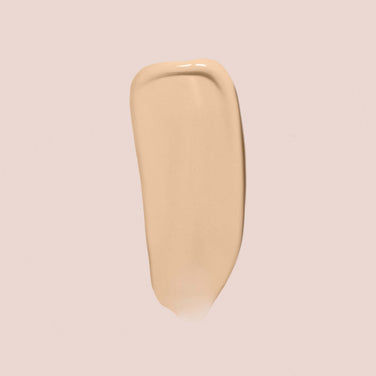  A smooth, elongated swatch of Jouer Cosmetics' Essential Crème Foundation in light beige is displayed on a light, neutral background. This paraben-free formula boasts a creamy texture with a slightly glossy finish, perfect for achieving an effortless look.