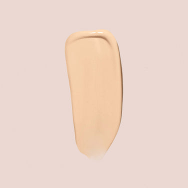  A swipe of Jouer Cosmetics Essential Crème Foundation on a light beige background showcases its smooth, creamy, and slightly glossy texture. This Paraben Free and Cruelty Free makeup product highlights its premium attributes while enhancing your natural beauty.