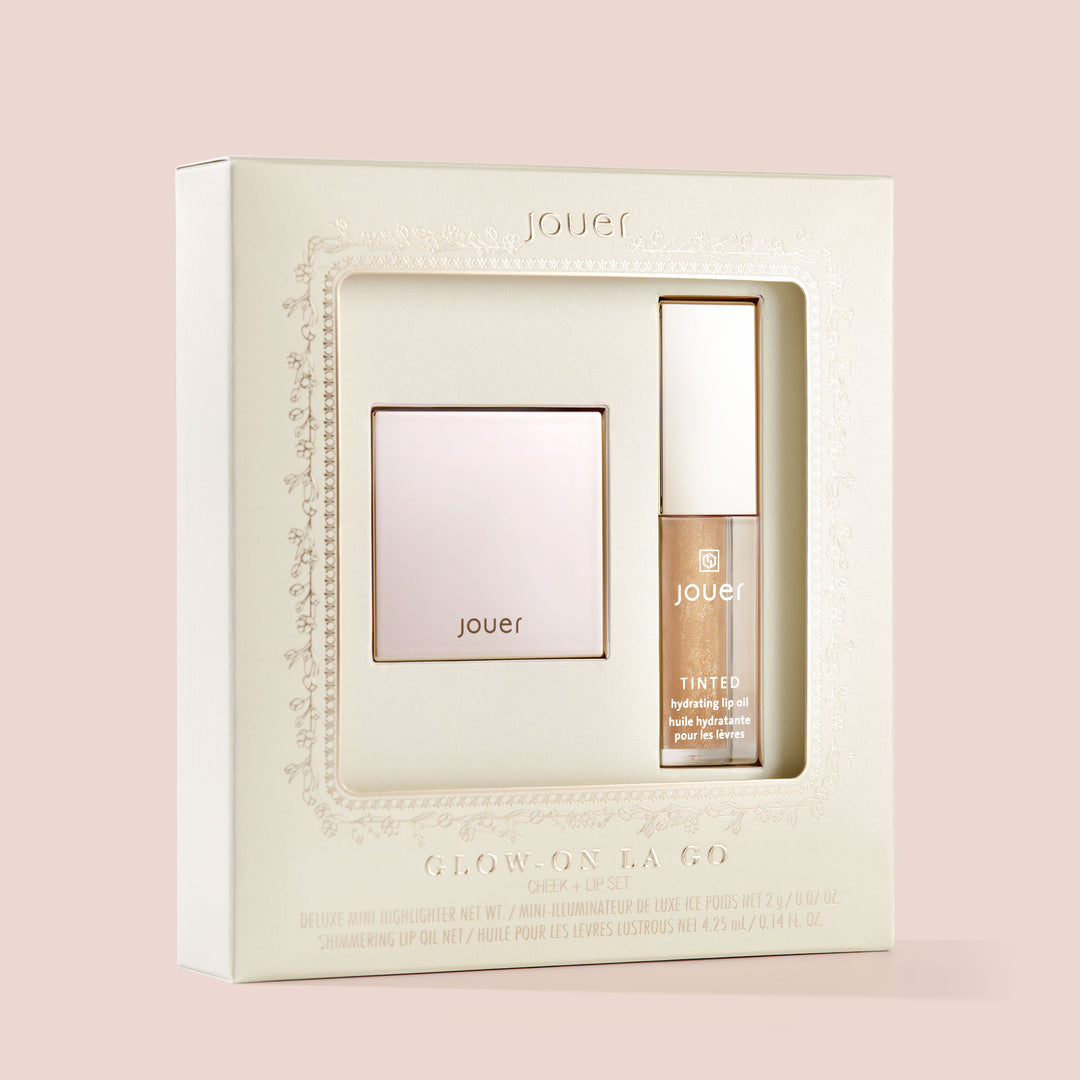 A beige package with a window showcasing a Jouer Cosmetics Glow-on La Go deluxe mini highlighter and a paraben-free tinted highlighter gel. The text on the box reads "Glow On the Go" and "Cheek + Lip Set". The products appear sleek and elegant, designed for enhancing cheeks and lips.