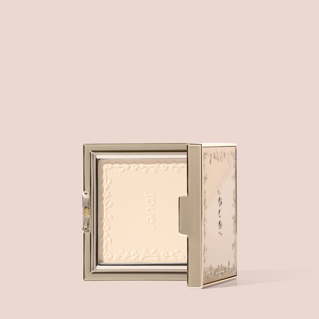 Open gold soft focus powder compact standing upright showing embossed powder inside