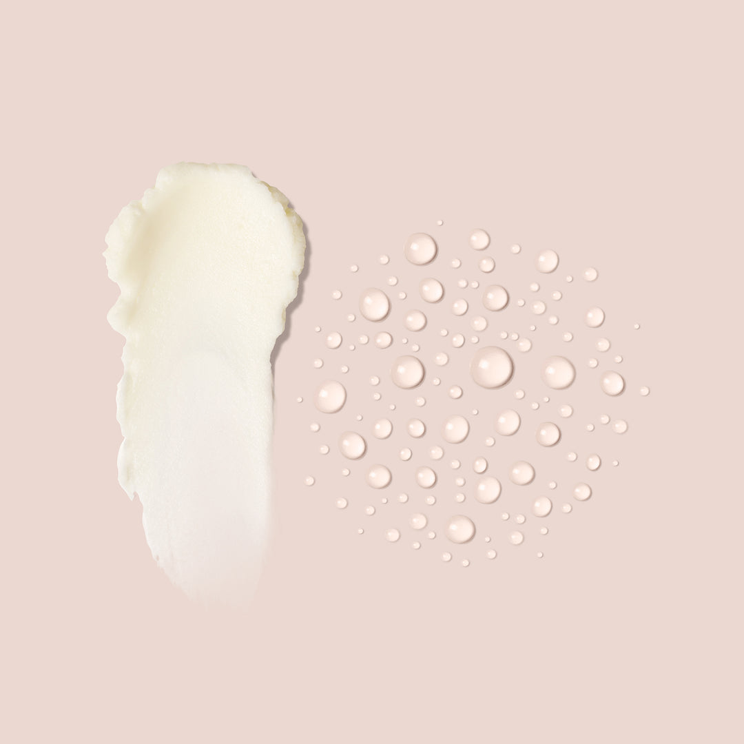 A smear of Hydrate & Repair creamy white lotion from Jouer Cosmetics is displayed on the left side of the image, while numerous small, spherical droplets resembling a moisture mist are scattered on the right side. Both are set against a light beige background.