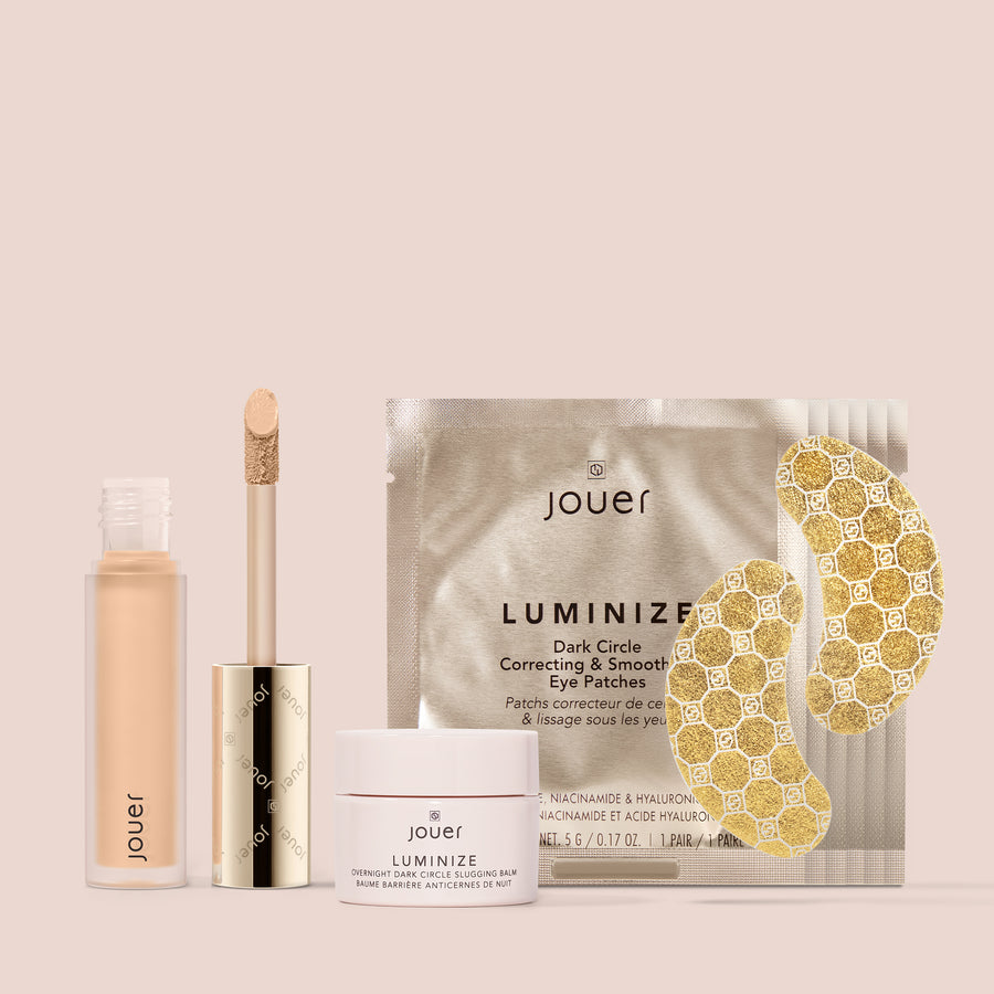 A collection of Jouer Cosmetics' Bright Eyes Set against a beige background, featuring a liquid concealer with an applicator wand, an anti-aging moisture primer in a small jar, and a pack of dark circle correcting and smoothing eye patches.