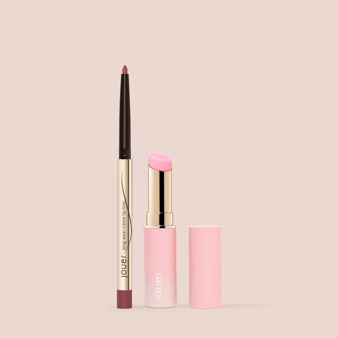 A gold and pink lip liner with a retractable tip is displayed standing upright beside a pink lipstick featuring a matching cap, both adorned with the "Jouer Cosmetics" branding against a light beige background. This La Vie En Rose Lip Kit is also paraben-free, ensuring safe and beautiful application every time.