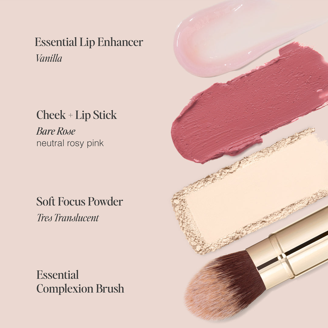 A set of cosmetic products arranged on a beige background. From top to bottom: a light pink lip gloss swatch labeled "Essential Lip Enhancer, Vanilla" (Cruelty-Free), a rosy pink cream swatch labeled "Cheek + Lip Stick, Bare Rose", a beige powder swipe labeled "Soft Focus Powder, Très Translucent" (Paraben-Free), and an angled makeup brush from the Les Must-Haves collection by Jouer Cosmetics.