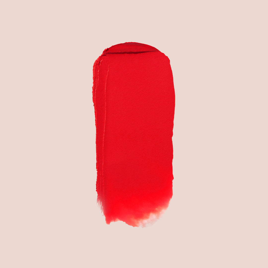 karma, A vertical swipe of Jouer Cosmetics' Balm Bouche lipstick in bold red hues stands out against a light beige background. The color ranges strikingly from top to bottom, with uneven, textured edges. This paraben-free formula guarantees a vibrant and safe application every time.