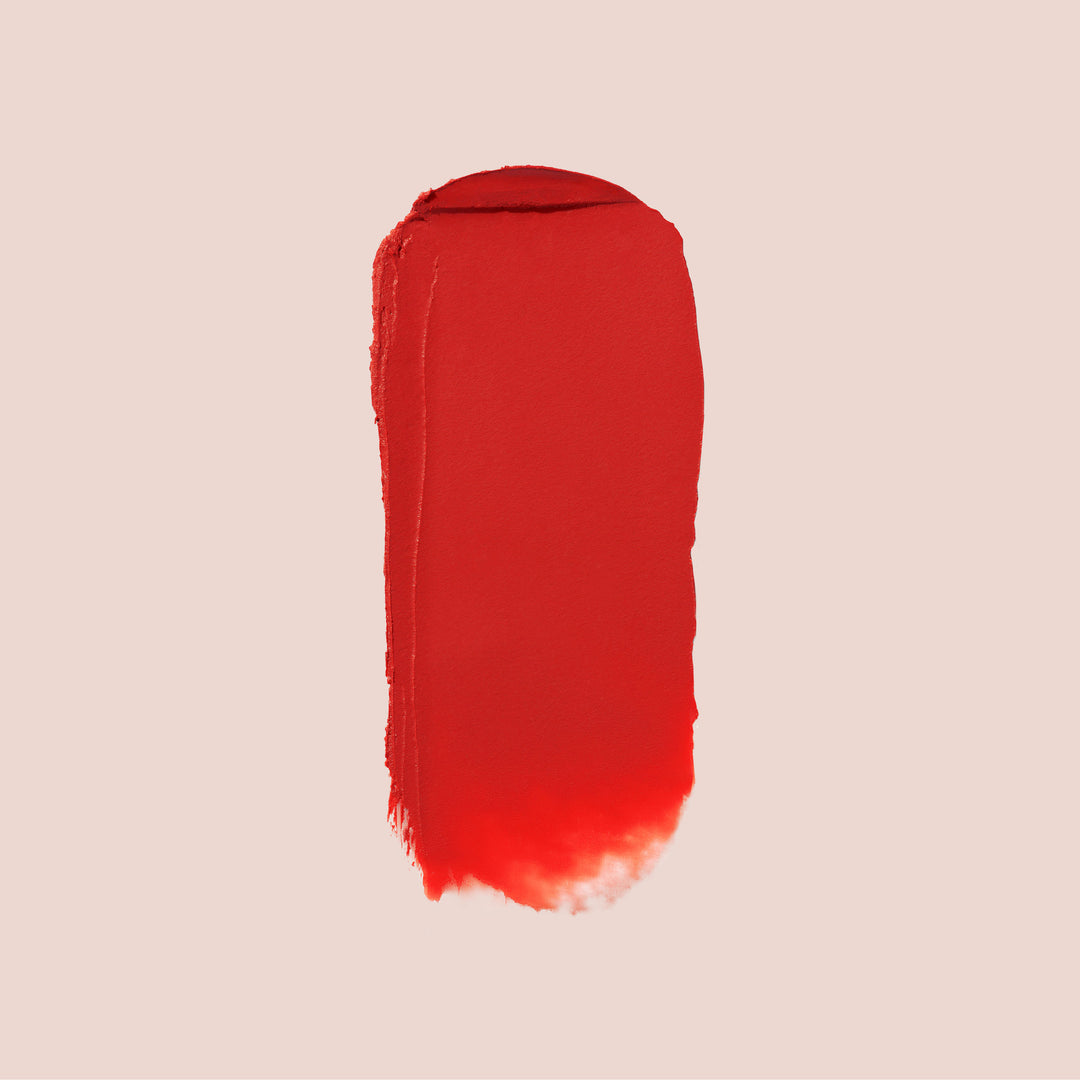 karma, A vertical swipe of Jouer Cosmetics' Balm Bouche lipstick in bold red hues stands out against a light beige background. The color ranges strikingly from top to bottom, with uneven, textured edges. This paraben-free formula guarantees a vibrant and safe application every time.