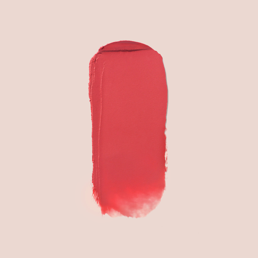Sensualite, A smear of Balm Bouche by Jouer Cosmetics, a deep rose vegan and paraben-free lipstick, is displayed on a neutral light pink background. The texture shows smooth but slightly uneven edges, with a deep rose color. The shade name is Sensualite.