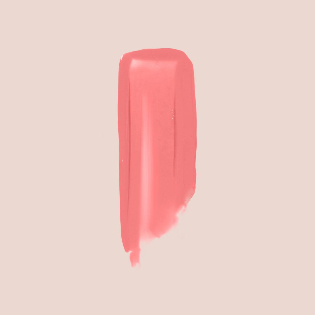 Peony, The Essential Shine Balm by Jouer Cosmetics creates a vertical smear of coral pink on a beige background, featuring smooth edges and a slightly uneven texture towards the bottom. This cruelty-free swipe showcases the balm's creamy consistency and vibrant color.