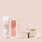 An arrangement of beauty products from Jouer Cosmetics' Mini Travel Set against a soft pink background. Included are a tube of Skin Barrier Cream on the left, a Mini Blush Bouquet, a clear Deluxe Mini Lip Oil, and a small square compact of shimmer highlighter.