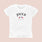 The Paris Meets LA Tee by Jouer Cosmetics is a white t-shirt crafted from 100% cotton. It features the word "Jouer" printed prominently in bold black letters at the chest, with an illustration of the American and French flags crossed below. Accompanying this design are the texts "French Beauty The LA Way" and "Est. 2008" underneath. The prewashed shirt has a light beige background and is machine washable in cold water.