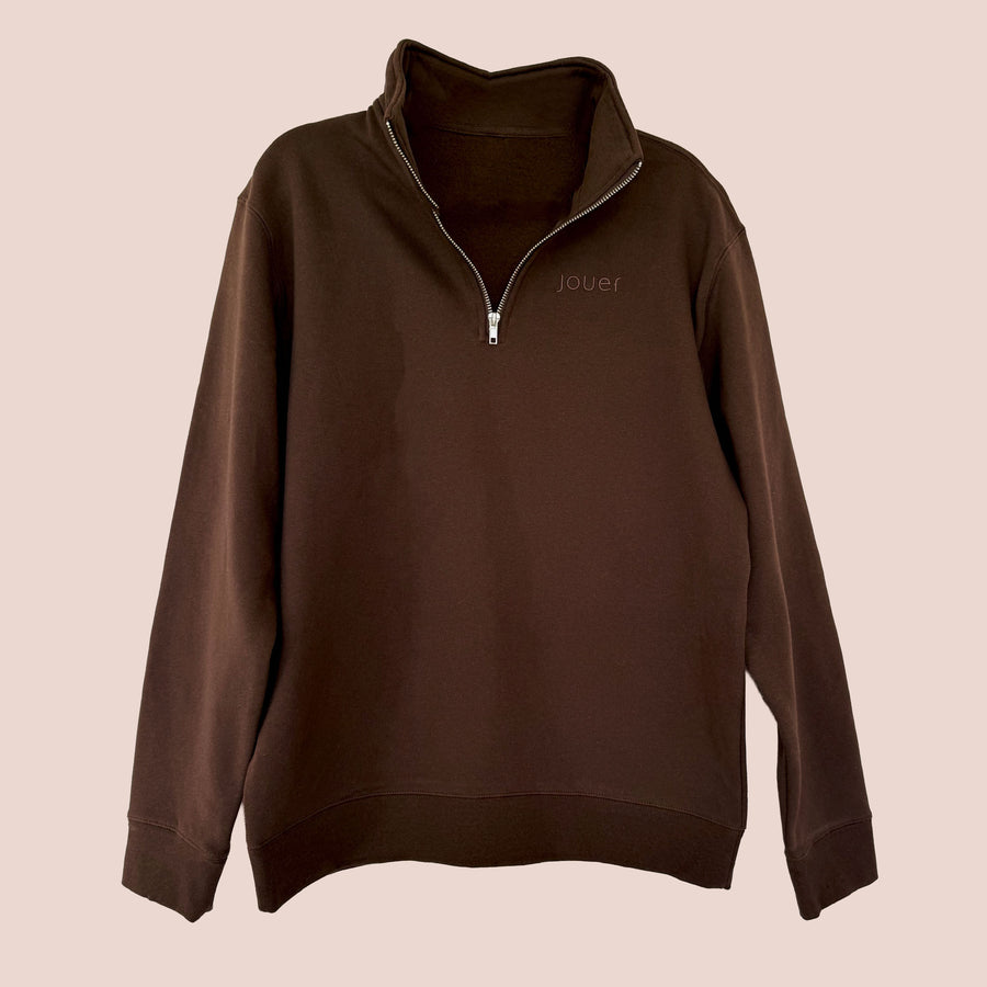 Jouer Quarter-Zip pullover in chocolate brown flat lay showing the embossed jouer logo and silver zipper on a beige background.