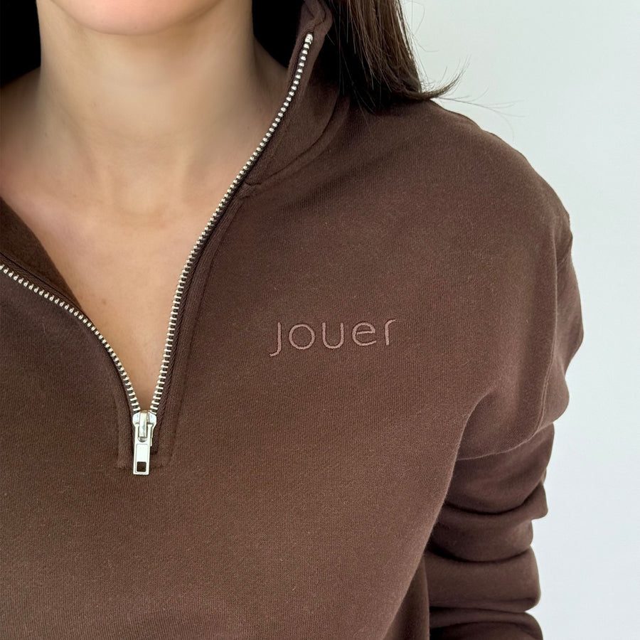 Close-up of Jouer Quarter-Zip pullover in chocolate brown showing the embossed jouer logo and silver zipper detail.