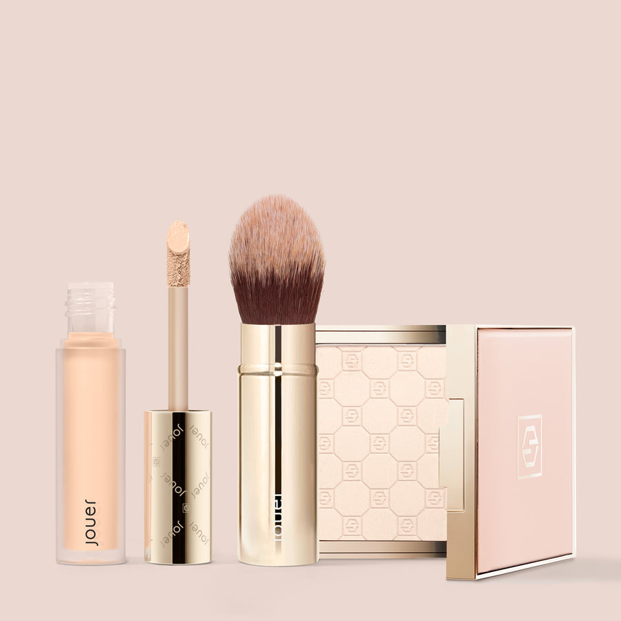 Jouer makeup complexion set with liquid concealer, powder compact, and brush on pink background