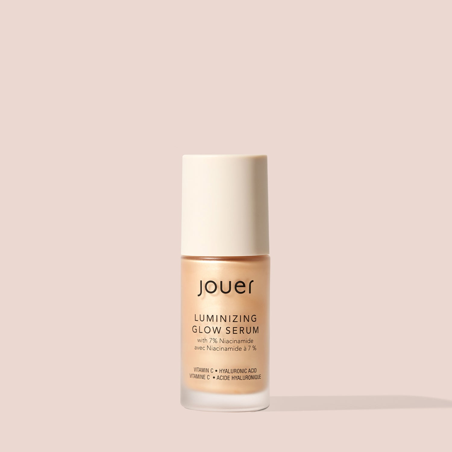 Nude face serum bottle labeled Jouer Luminizing Glow Serum with niacinamide, vitamin C, and hyaluronic acid on neutral background.