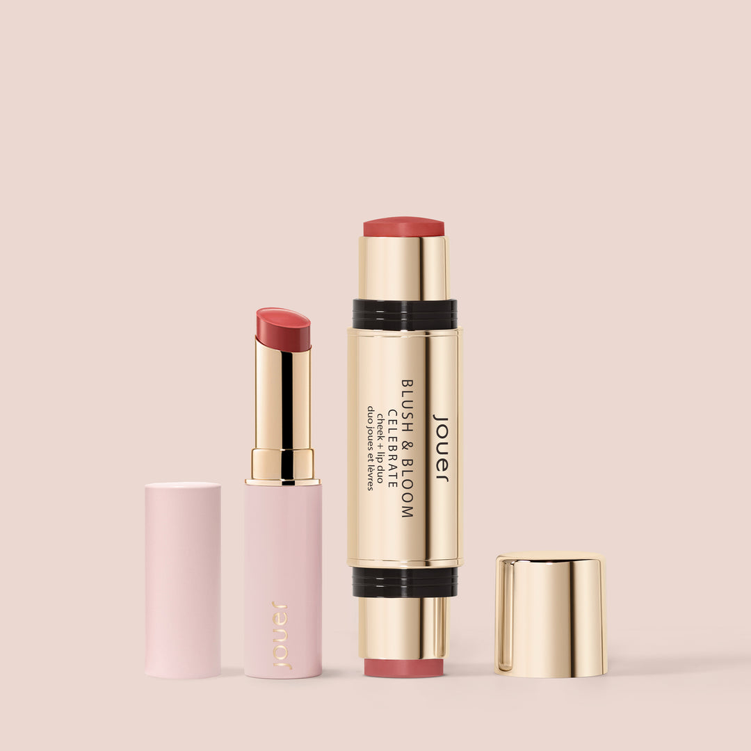Jouer Blush & Bloom Cheek + Lip Duo and matching hydrating lip balm standing upright on a soft blush pink background, lids removed to show the product shades.