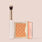Jouer Precision Brightening Set in Orange with a warm copper-toned embossed powder compact and Jouer tapered brush.